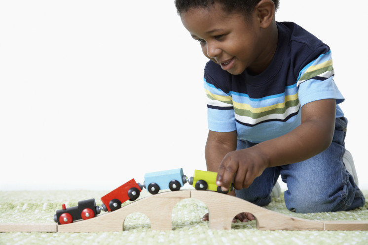 Ein kleiner Junge spielt mit einer Holzeisenbahn.